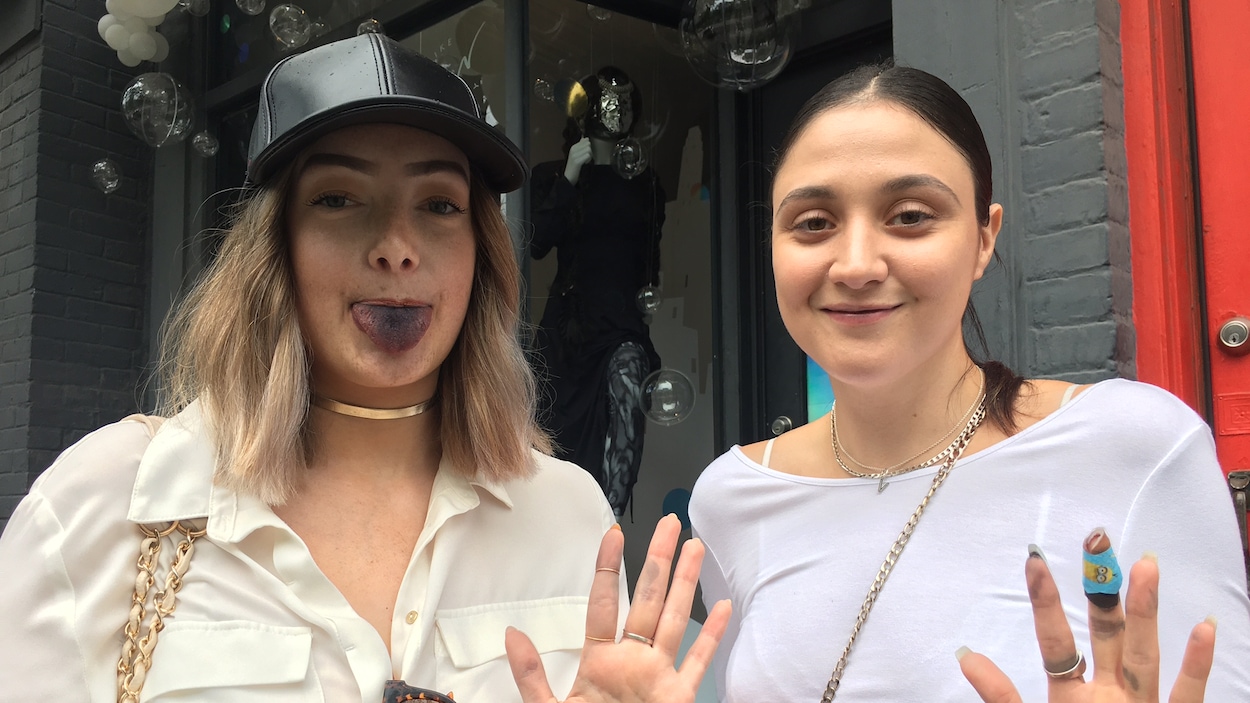 Deux jeunes femmes posent en tirant la langue et en montrant leurs doigts tachés par la crème glacée au charbon actif