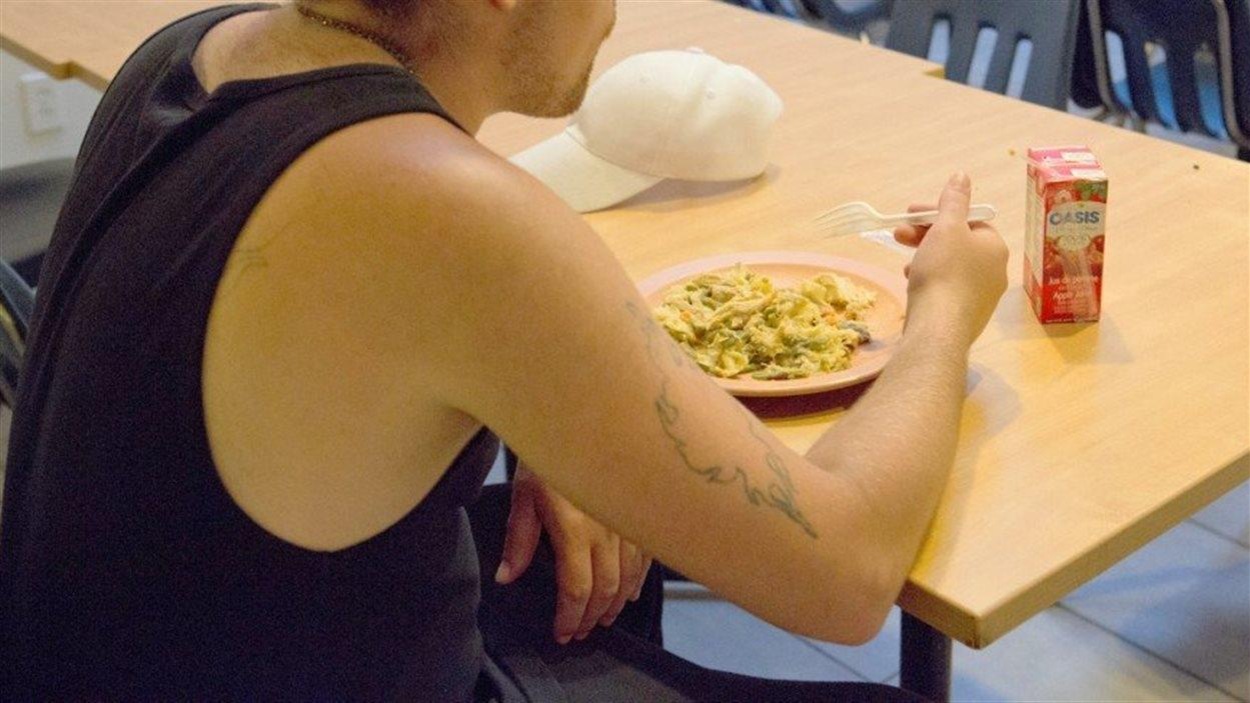 Une jeune home est assis à une table et mange un repas avec une fourchette de plastique. Une jeune home est assis à une table et mange un repas avec une fourchette de plastique.