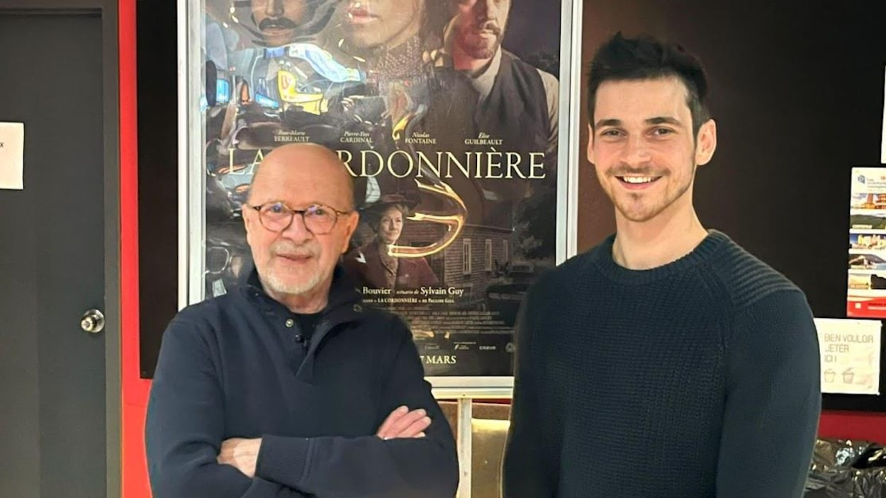 Deux hommes vêtus de chandails sombres, prennent la pose devant l'affiche d'un film. Deux hommes vêtus de chandails sombres, prennent la pose devant l'affiche d'un film.