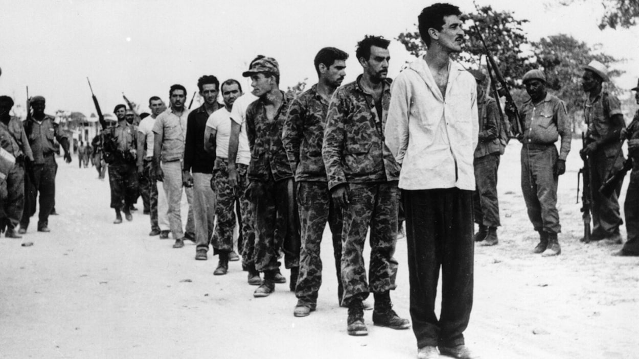 Une série d'hommes les mains liées défile devant des militaires cubains. Une série d'hommes les mains liées défile devant des militaires cubains.