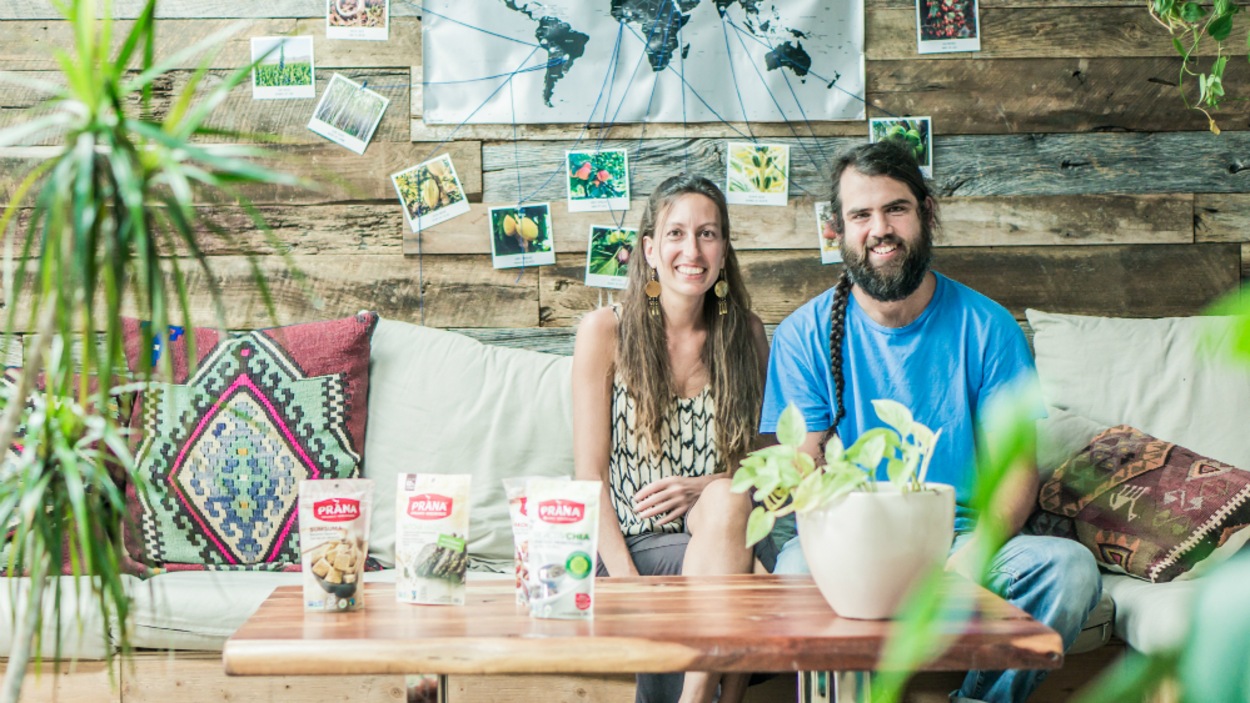 Le couple est assis sur un divan devant une table basse sur laquelle sont posés des sacs de collation Prana. Le couple est assis sur un divan devant une table basse sur laquelle sont posés des sacs de collation Prana.