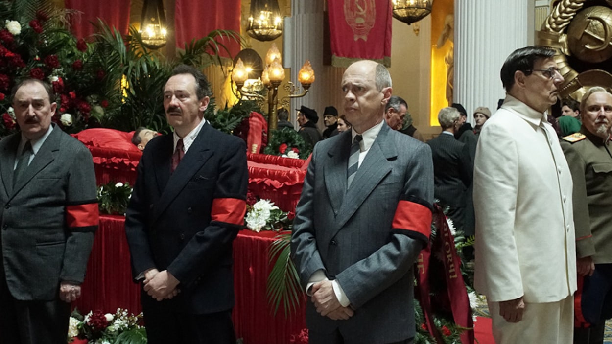 Quatre hommes portant des brassards rouges entourent un cercueil tendu de satin rouge dans une representation tirée du film<i>La mort de Staline</i>, d'Armando Iannucci Quatre hommes portant des brassards rouges entourent un cercueil tendu de satin rouge dans une representation tirée du film<i>La mort de Staline</i>, d'Armando Iannucci