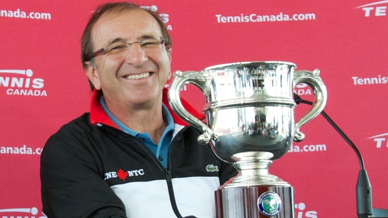 Il est assis à une table sur laquelle est déposé un trophée argenté. Il est assis à une table sur laquelle est déposé un trophée argenté.