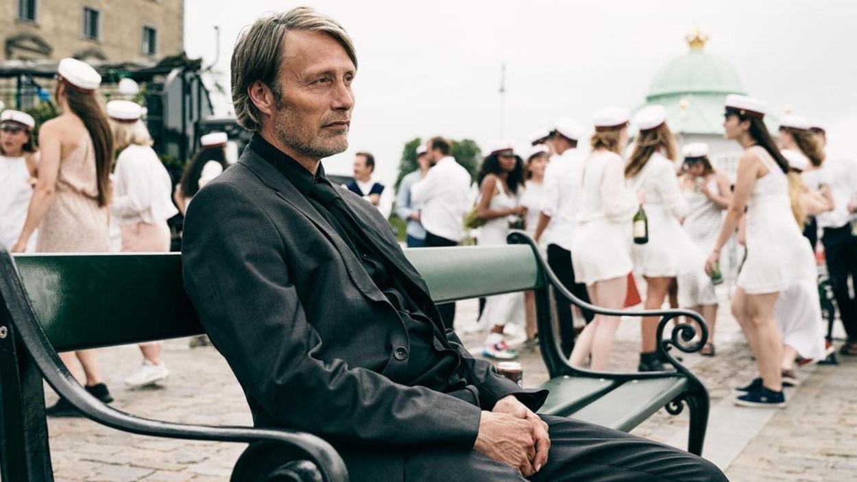 Un homme (Mads Mikkelsen) assis seul sur un banc, au milieu d'une fête. Un homme (Mads Mikkelsen) assis seul sur un banc, au milieu d'une fête.