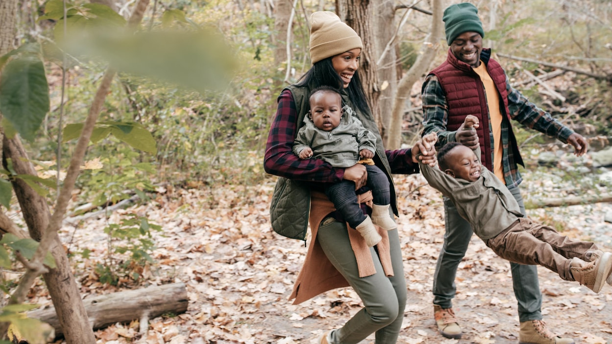 Un couple, accompagné de leurs deux jeunes enfants, marchent dans la forêt, où la plupart des feuilles sont tombées sur le sol. Un couple, accompagné de leurs deux jeunes enfants, marchent dans la forêt, où la plupart des feuilles sont tombées sur le sol.