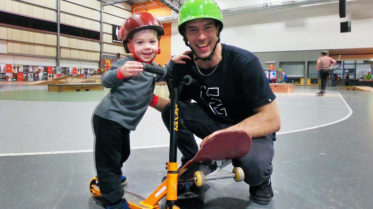 Un père en planche à roulettes pose en souriant avec son fils en trottinette. Un père en planche à roulettes pose en souriant avec son fils en trottinette.
