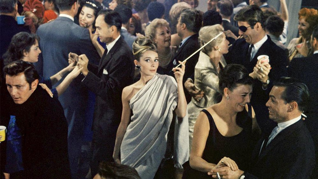 Une femme en tenue de soirée avec un porte cigarette au milieu de gens dansant et riant. Une femme en tenue de soirée avec un porte cigarette au milieu de gens dansant et riant.