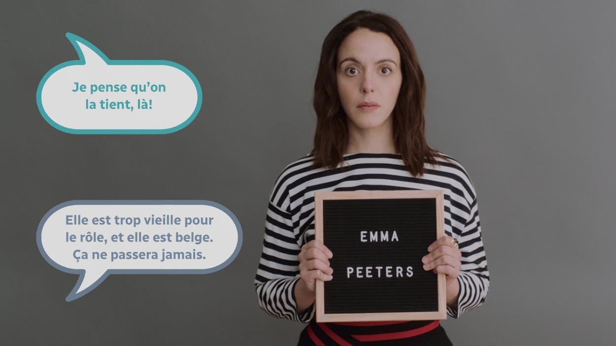 Une jeune femme (Monia Chokri) portant une affichette avec le nom Emma Peeters écrit dessus. Une jeune femme (Monia Chokri) portant une affichette avec le nom Emma Peeters écrit dessus.