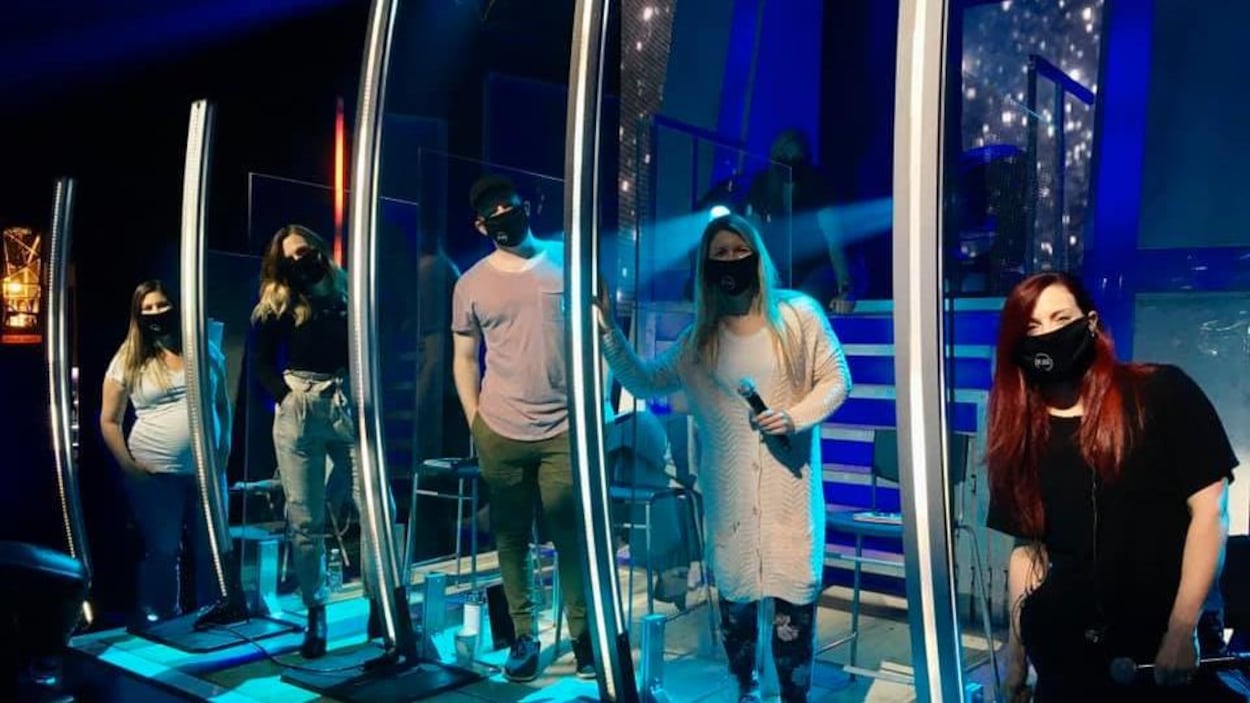 Sur le plateau d'En direct de l'univers, cinq choristes, avec couvre-visage, sont dans des cages de plexiglas. Sur le plateau d'En direct de l'univers, cinq choristes, avec couvre-visage, sont dans des cages de plexiglas.