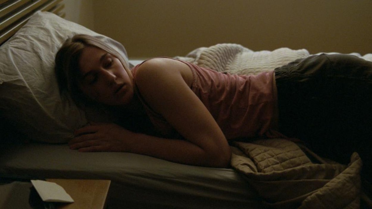 Une jeune femme (Mylène Mackay) allongée sur le côté, sur un lit.