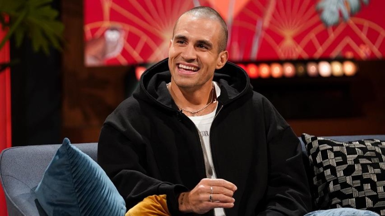 Un homme qui sourit. Il porte un t-shirt blanc et un blouson noir.