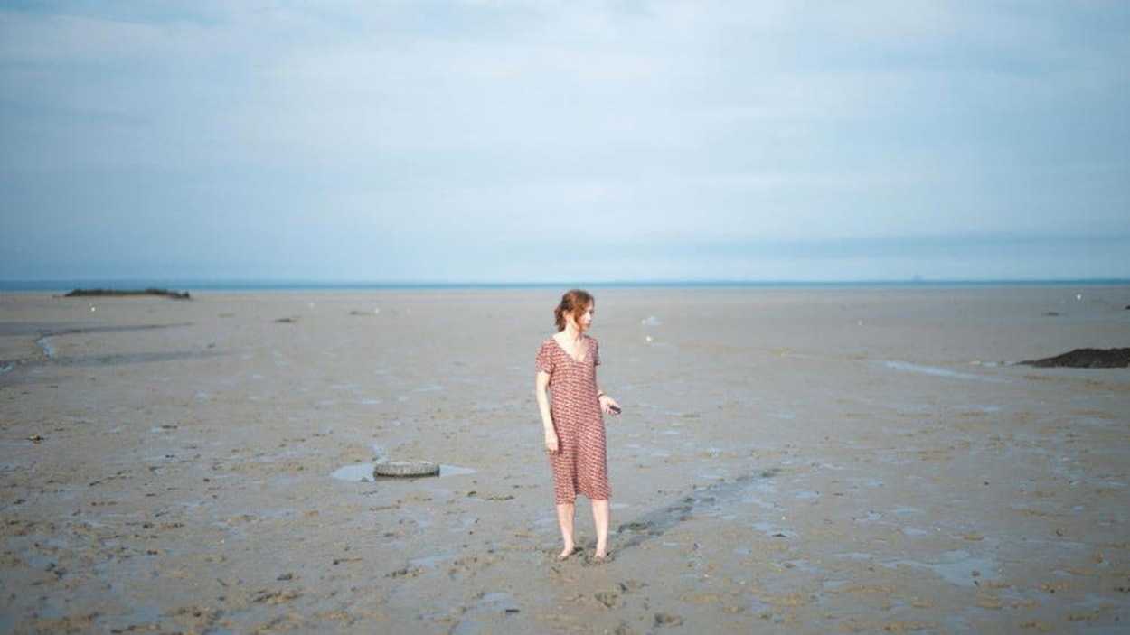A woman in a dress (Isabelle Huppert) alone on a beach at low tide.