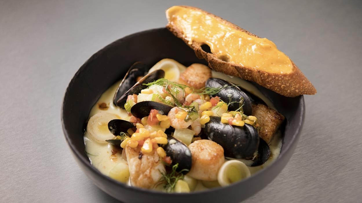 Un bol de chaudrée de fruits de mer et poissons, salsa de maïs et tomate accompagné d'un croûton à l’aïoli. Un bol de chaudrée de fruits de mer et poissons, salsa de maïs et tomate accompagné d'un croûton à l’aïoli.