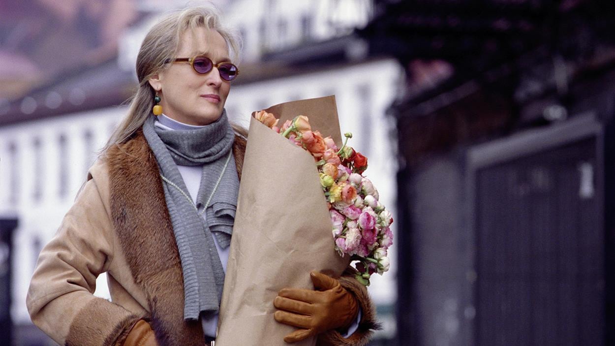 Une femme (Meryl Streep) portant un manteau et des gants tient un bouquet de fleurs dans ses mains