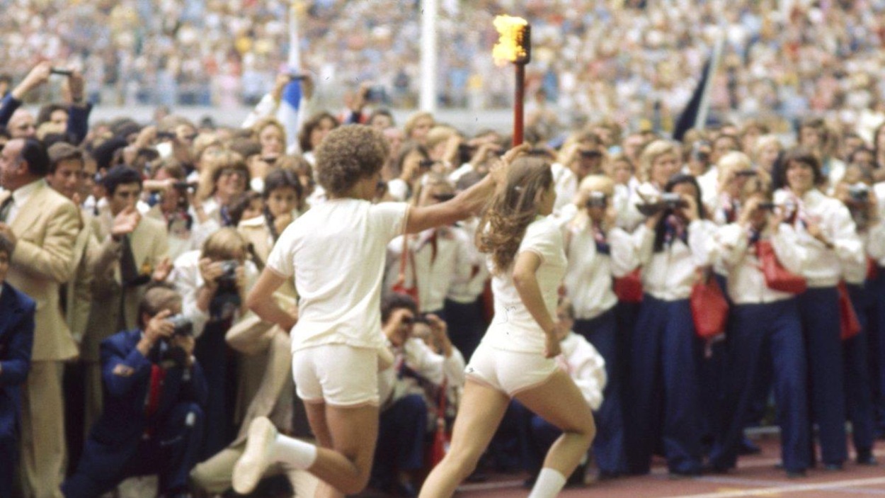 Un homme et une femme en tenue blanche courent sur une piste en portant la flamme olympique. Un homme et une femme en tenue blanche courent sur une piste en portant la flamme olympique.