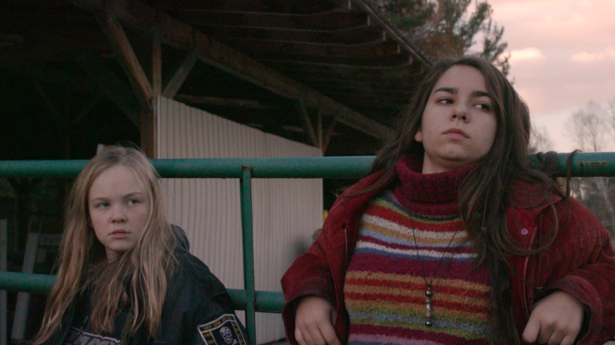 Deux jeunes filles, à l'extérieur, adossées contre une clôture. Deux jeunes filles, à l'extérieur, adossées contre une clôture.