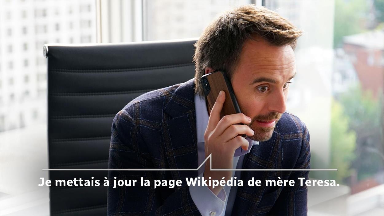 Un homme (Louis-José Houde) au téléphone et le dialogue écrit: Je mettais à jour la page Wikipédia de mère Teresa.