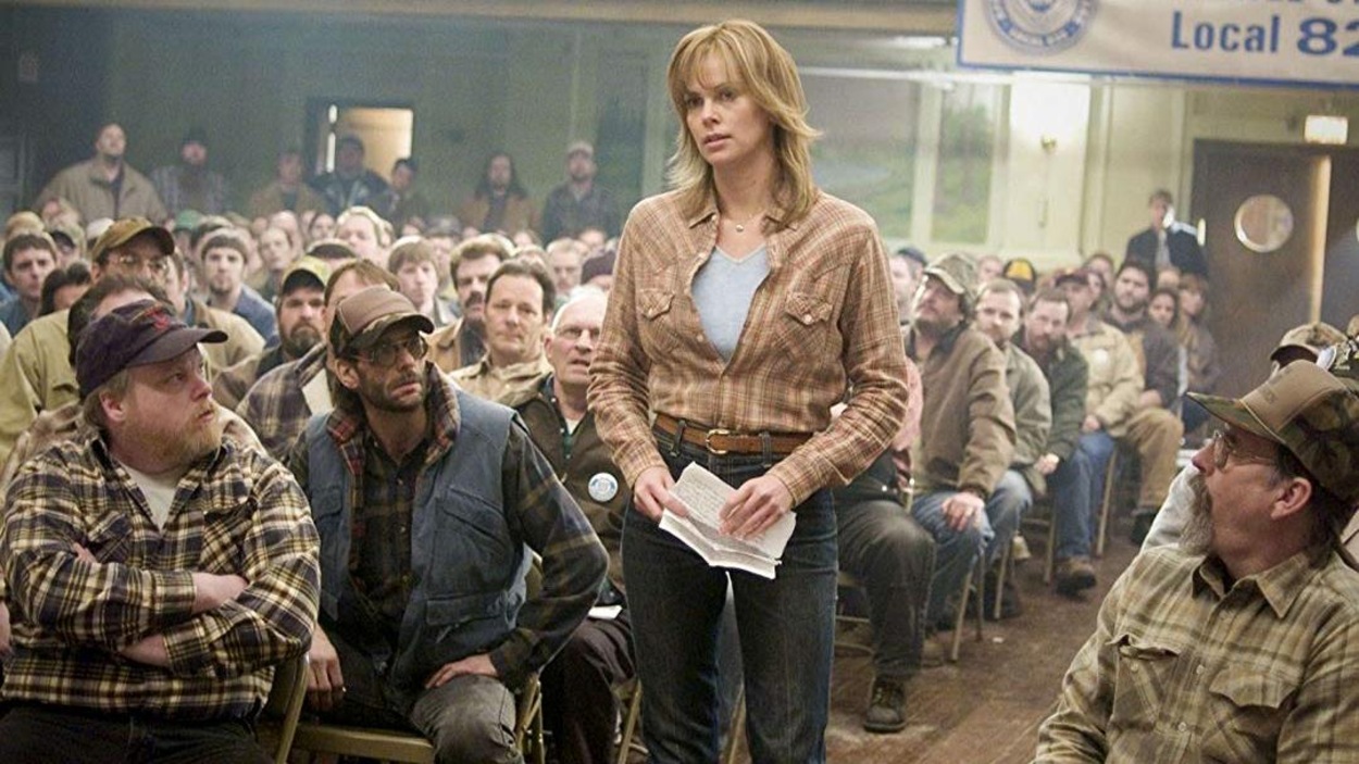 Une femme (Charlize Theron) en jeans et chemise carrottée, debout au milieu d'une assemblée d'hommes assis. Une femme (Charlize Theron) en jeans et chemise carrottée, debout au milieu d'une assemblée d'hommes assis.
