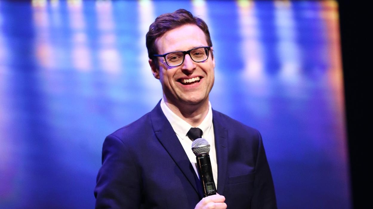 Un jeune homme à lunettes, souriant, un micro à la main Un jeune homme à lunettes, souriant, un micro à la main