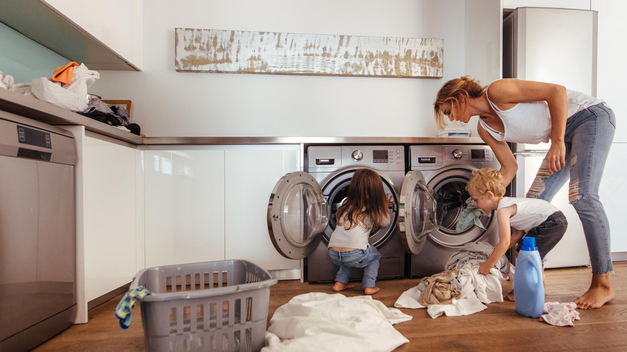 Une mère et ses deux enfants remplissent une laveuse de vêtements. Une mère et ses deux enfants remplissent une laveuse de vêtements.