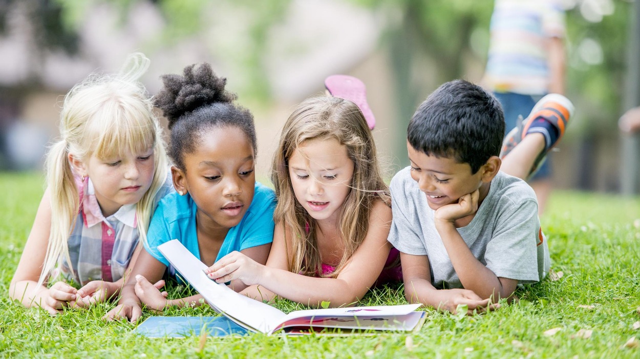 Quatre enfants allongés dans le gazon sont en train de lire un livre. Quatre enfants allongés dans le gazon sont en train de lire un livre.