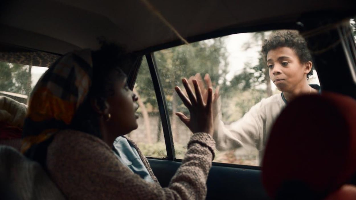 Un jeune garçon et une femme collent leur main, chacun d'un côté d'une vitre de voiture.