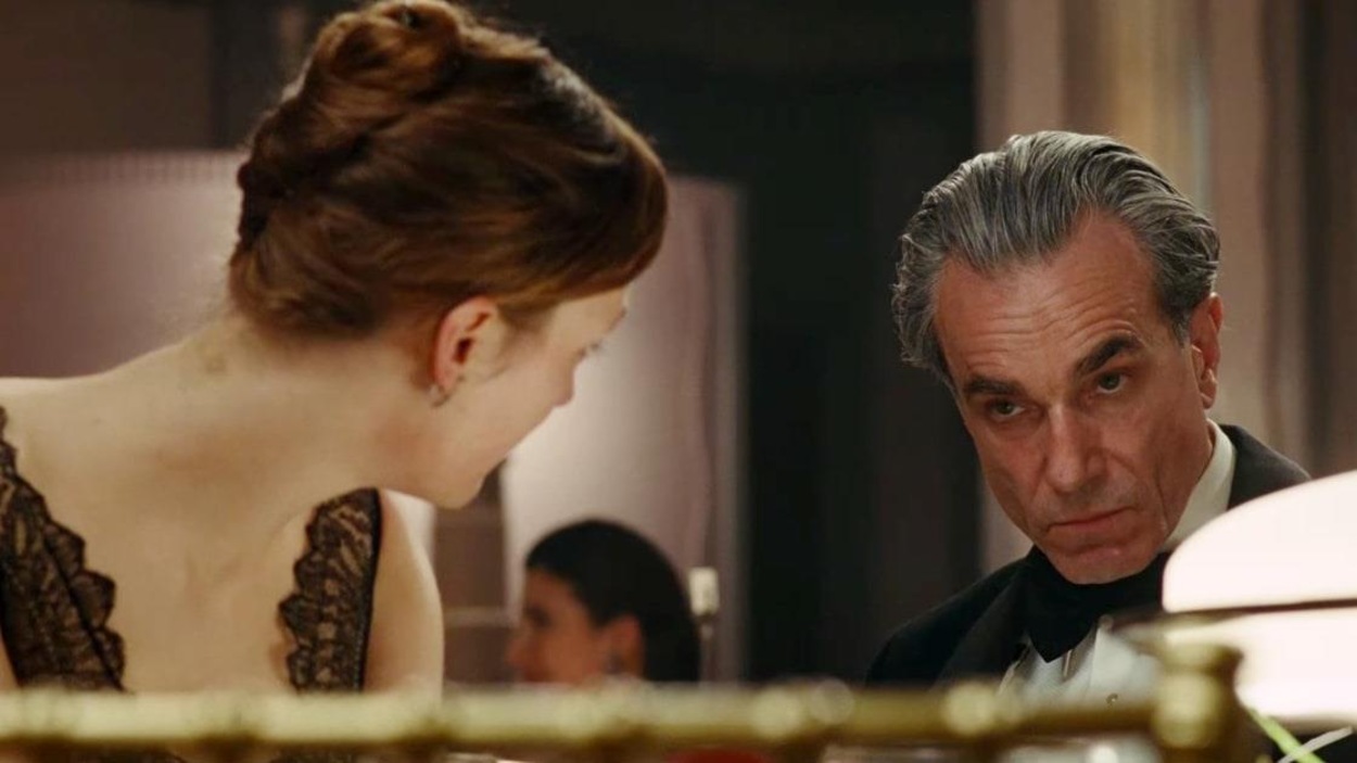 Un homme aux cheveux gris, l'air sévère, regardé par une femme en robe, de dos Un homme aux cheveux gris, l'air sévère, regardé par une femme en robe, de dos