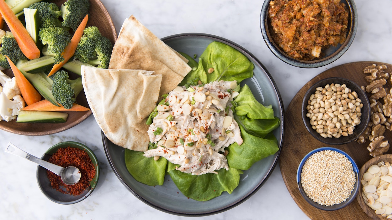 Plusieurs plats de sauce, de poulet, de crudités et de divers ingrédients sont sur le comptoir.