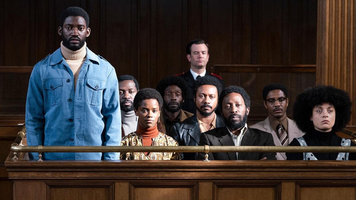 Plusieurs hommes et femmes noirs, dans un box d'accusés au tribunal, dont l'un se tient debout. Plusieurs hommes et femmes noirs, dans un box d'accusés au tribunal, dont l'un se tient debout.