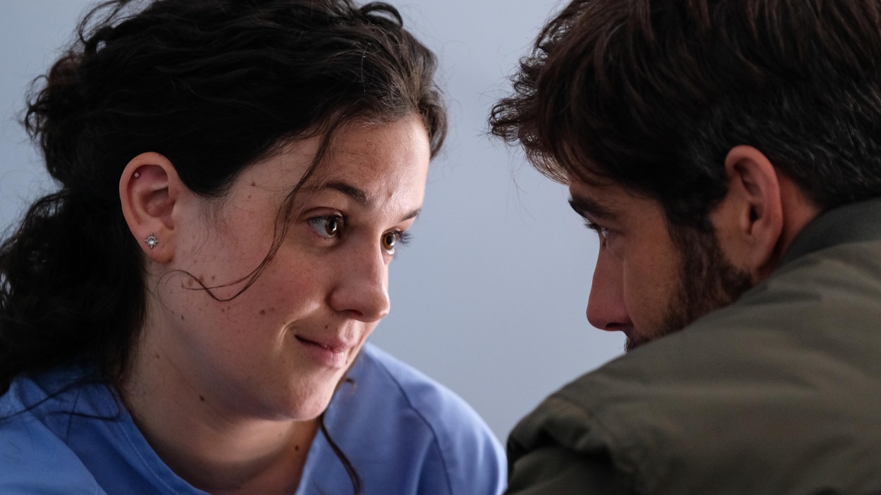 Une jeune femme en jaquette d'hôpital regarde son amoureux dans les yeux.