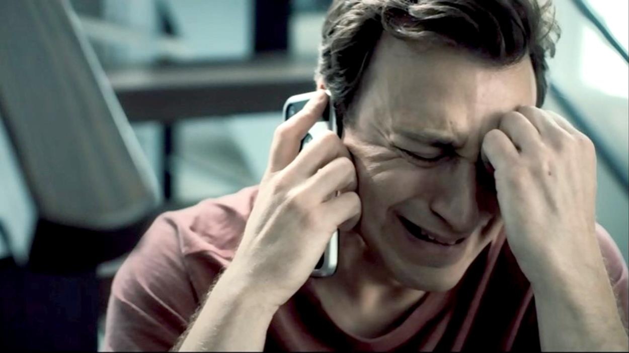 Assis dans les escaliers, Sébastien (Benoît McGinnis) éclate en sanglots en parlant au téléphone.