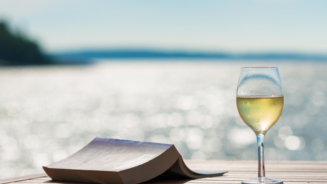 Un livre et un verre de vin blanc sont posés sur une table à l'extérieur Un livre et un verre de vin blanc sont posés sur une table à l'extérieur