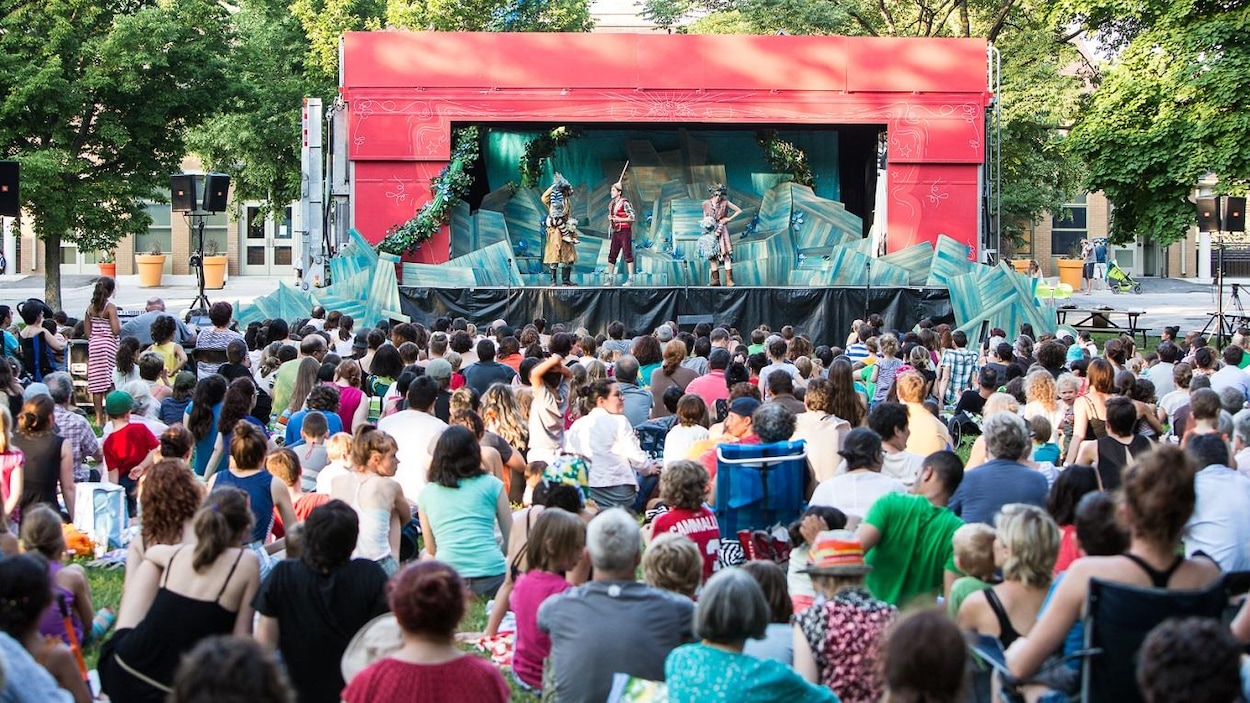 Une foule d'enfants et leurs parents sont assis dans un parc devant une scène de théâtre. Une foule d'enfants et leurs parents sont assis dans un parc devant une scène de théâtre.