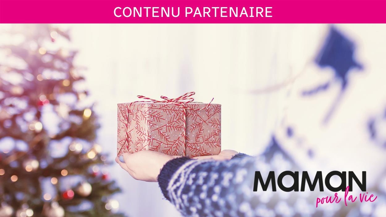 Contenue partenaire Maman pour la vie : deux mains portent un cadeau vers un arbre de Noël en arrière-plan. Contenue partenaire Maman pour la vie : deux mains portent un cadeau vers un arbre de Noël en arrière-plan.