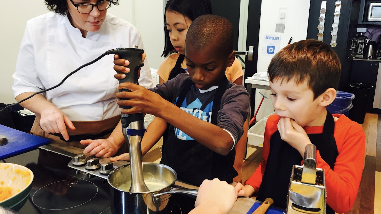 Avec ses camarades, un jeune garçon passe sa sauce au pied mélangeur sous l'oeil averti d'une cheffe cuisinière. Avec ses camarades, un jeune garçon passe sa sauce au pied mélangeur sous l'oeil averti d'une cheffe cuisinière.