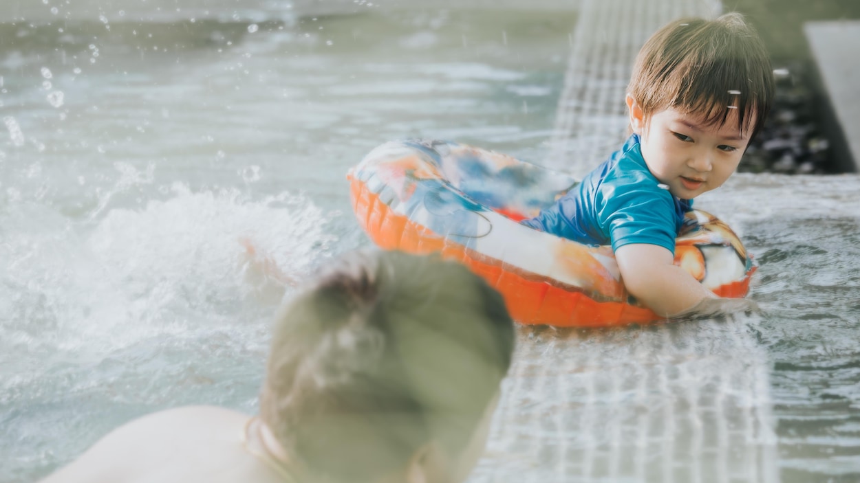 Un petit garçon est dans une bouée à la piscine, il regarde son papa. Les deux sont d'origine asiatique. Un petit garçon est dans une bouée à la piscine, il regarde son papa. Les deux sont d'origine asiatique.