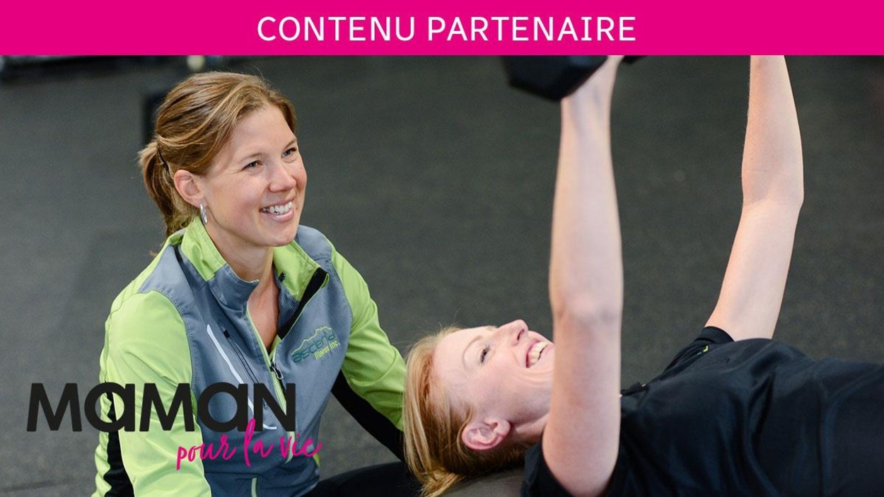 La femme est allongée et soulève des poids, elle sourit. Son entraîneuse l'encourage. La femme est allongée et soulève des poids, elle sourit. Son entraîneuse l'encourage.