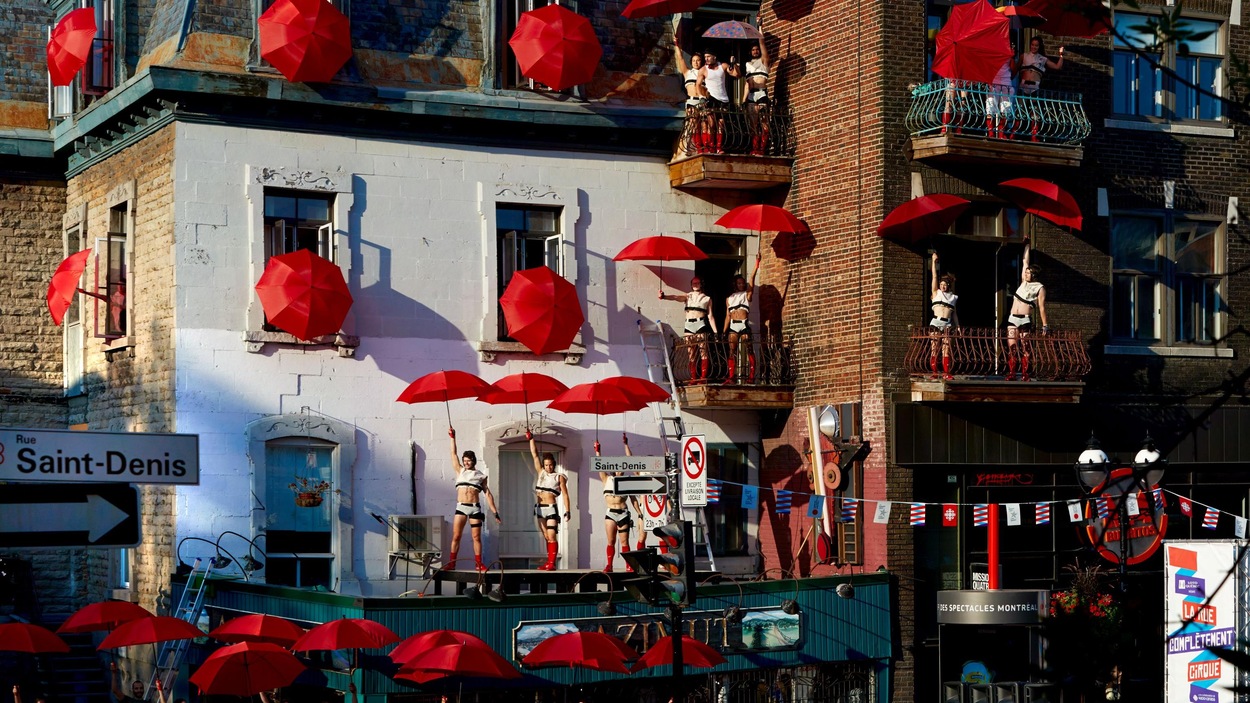 Des acrobates et des parapluies rouges sur la rue Saint-Denis, sur les balcons et sur les toits Des acrobates et des parapluies rouges sur la rue Saint-Denis, sur les balcons et sur les toits