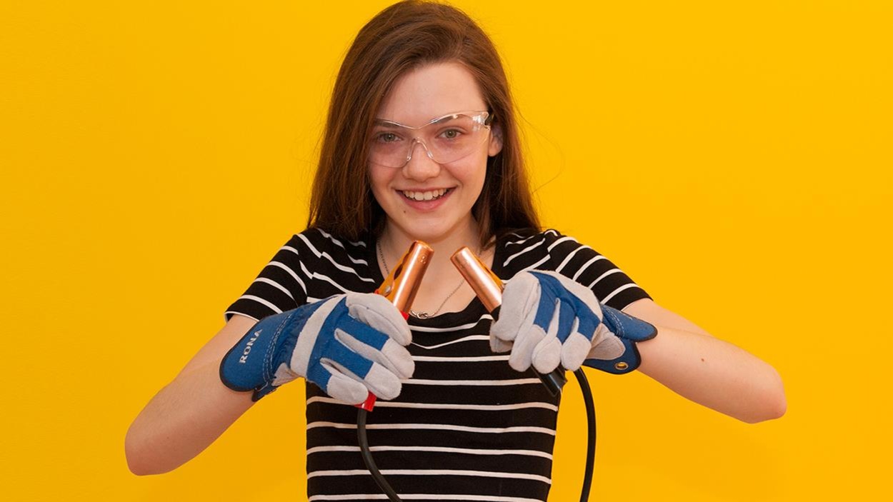 Sur un fond jaune, Jade porte des lunettes de sécurité et des gants de construction. Elle tient dans ses mains des câbles de démarrage. Sur un fond jaune, Jade porte des lunettes de sécurité et des gants de construction. Elle tient dans ses mains des câbles de démarrage.
