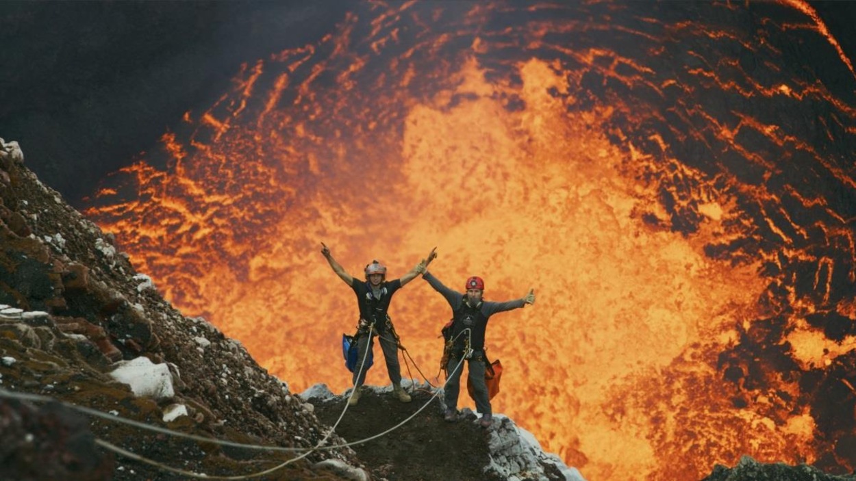 On voit le volcan en éruption et les deux hommes attachés à des cordes. On voit le volcan en éruption et les deux hommes attachés à des cordes.