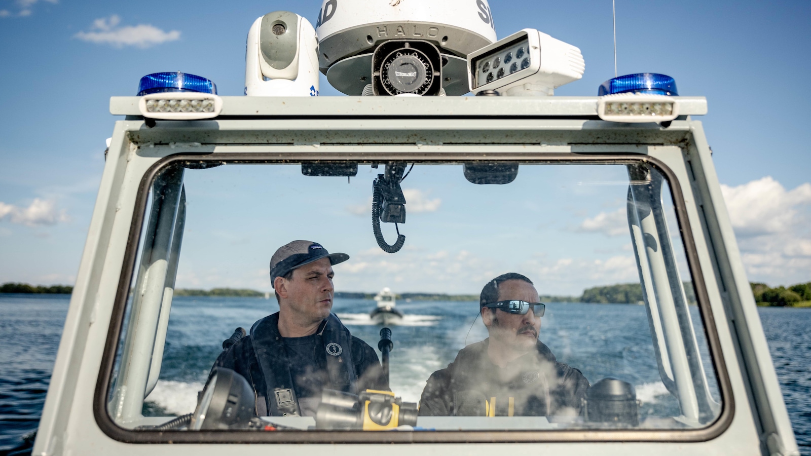 Deux hommes naviguent dans un bateau de police sur un cours d'eau. 