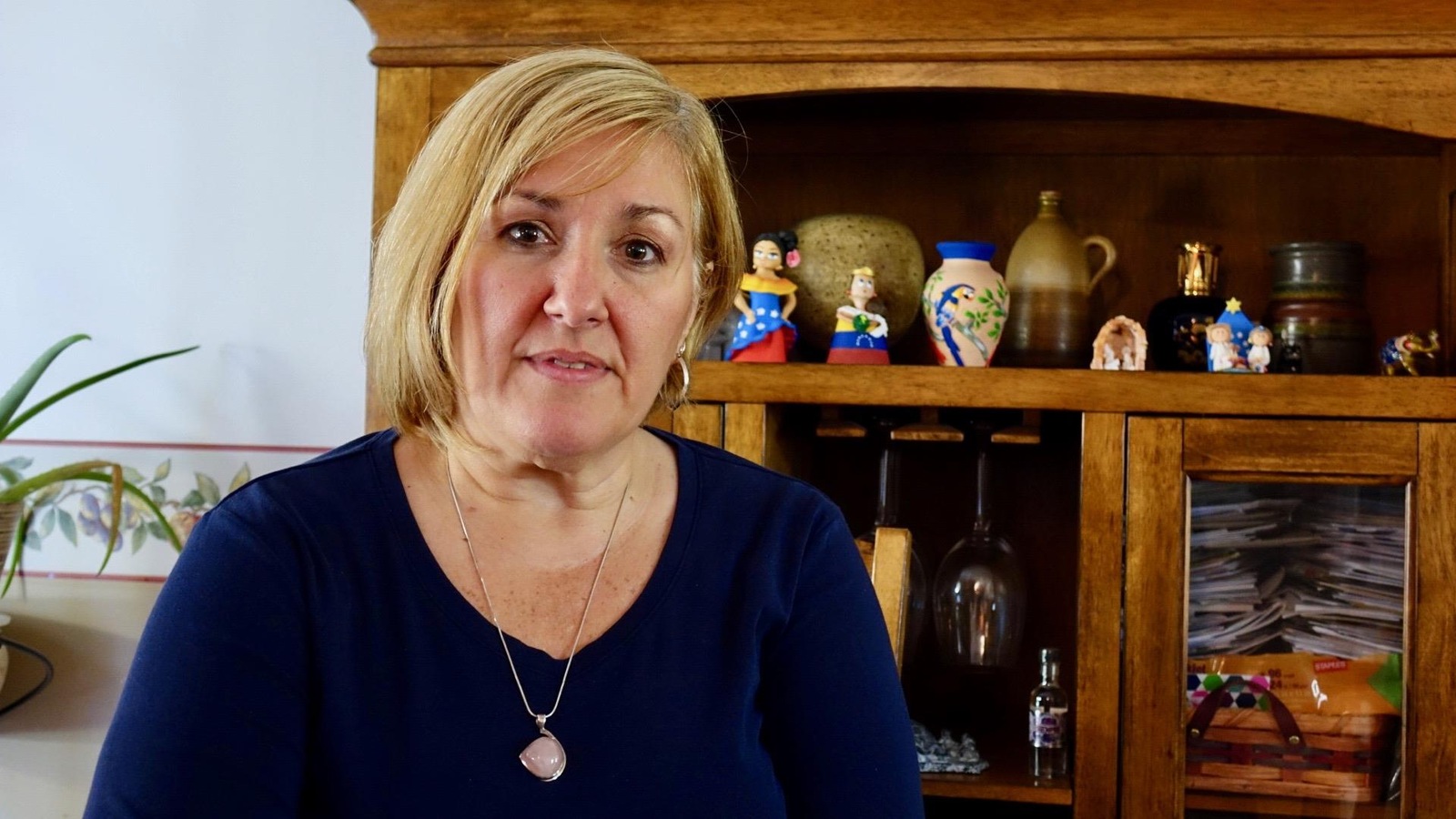 Une femme photographiée dans sa salle à manger. En arrière-plan, un meuble sur lequel on peut voir des figurines du Venezuela Une femme photographiée dans sa salle à manger. En arrière-plan, un meuble sur lequel on peut voir des figurines du Venezuela