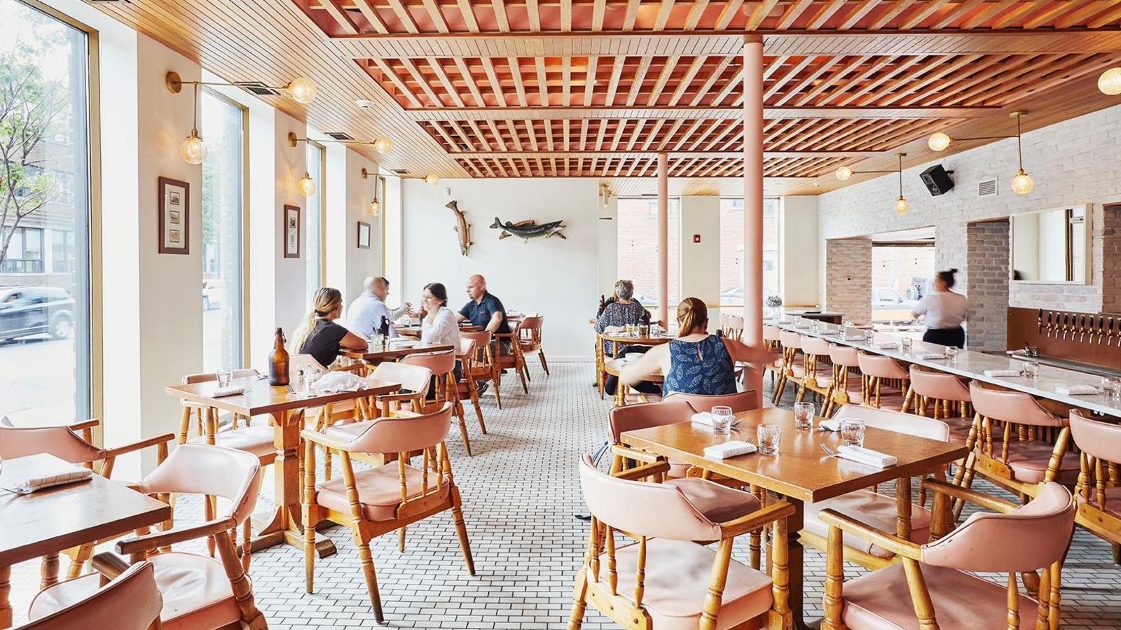 Des gens sont assis à des tables à l'intérieur d'une grande salle avec un long comptoir en plein jour dans la brasserie. Des gens sont assis à des tables à l'intérieur d'une grande salle avec un long comptoir en plein jour dans la brasserie.