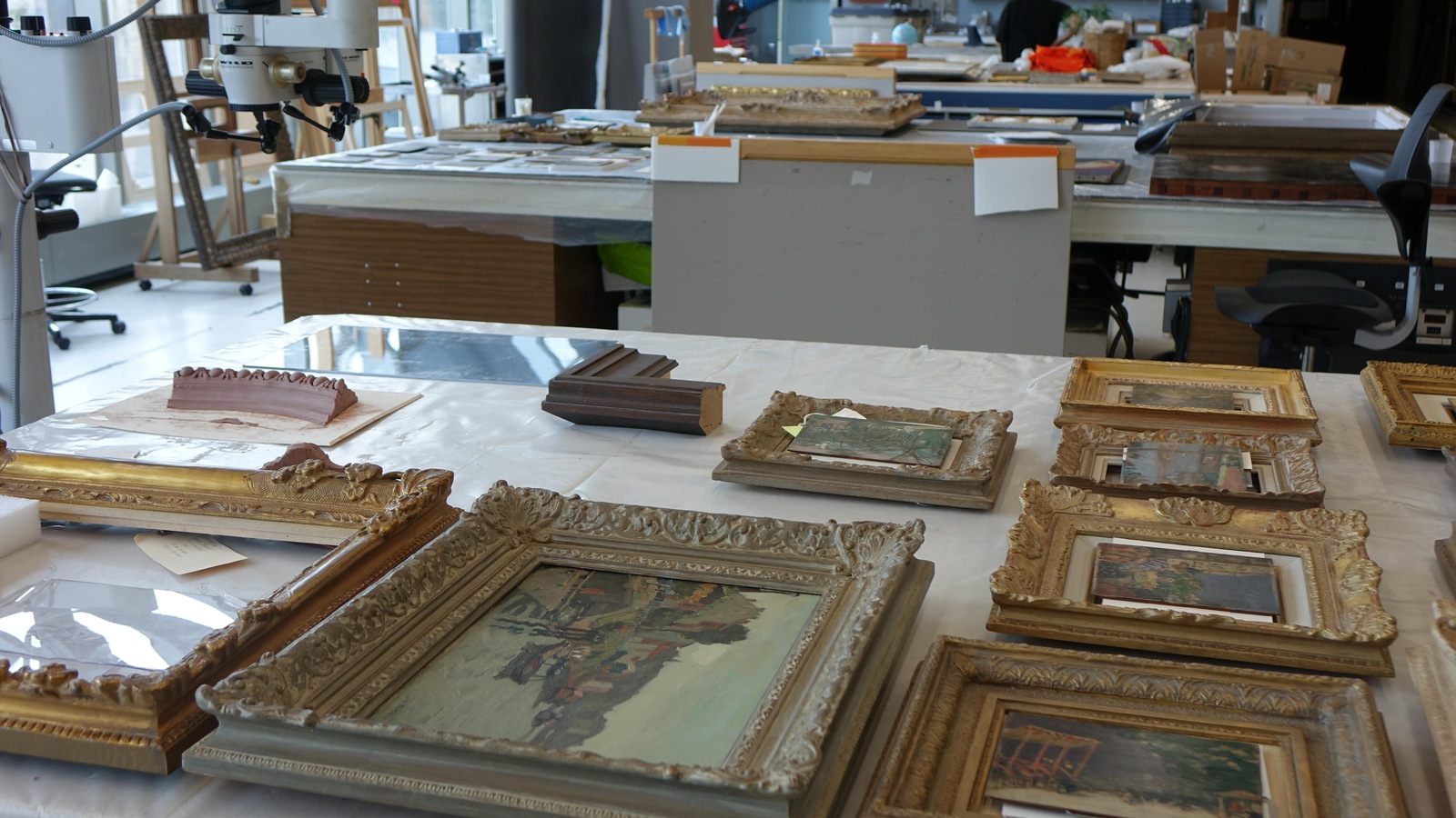Des oeuvres encadrées sont déposées sur une table dans un atelier. Des oeuvres encadrées sont déposées sur une table dans un atelier.
