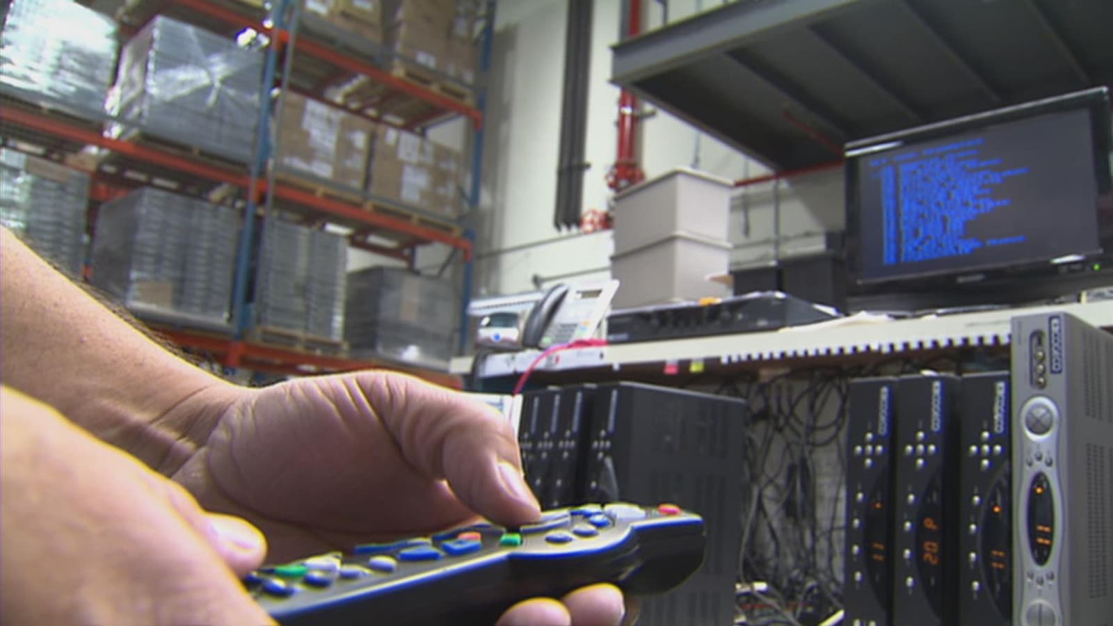 Une main tenant une télécommande de Cogeco devant un écran et de l'équipement des différents services offerts par l'entreprise. Une main tenant une télécommande de Cogeco devant un écran et de l'équipement des différents services offerts par l'entreprise.
