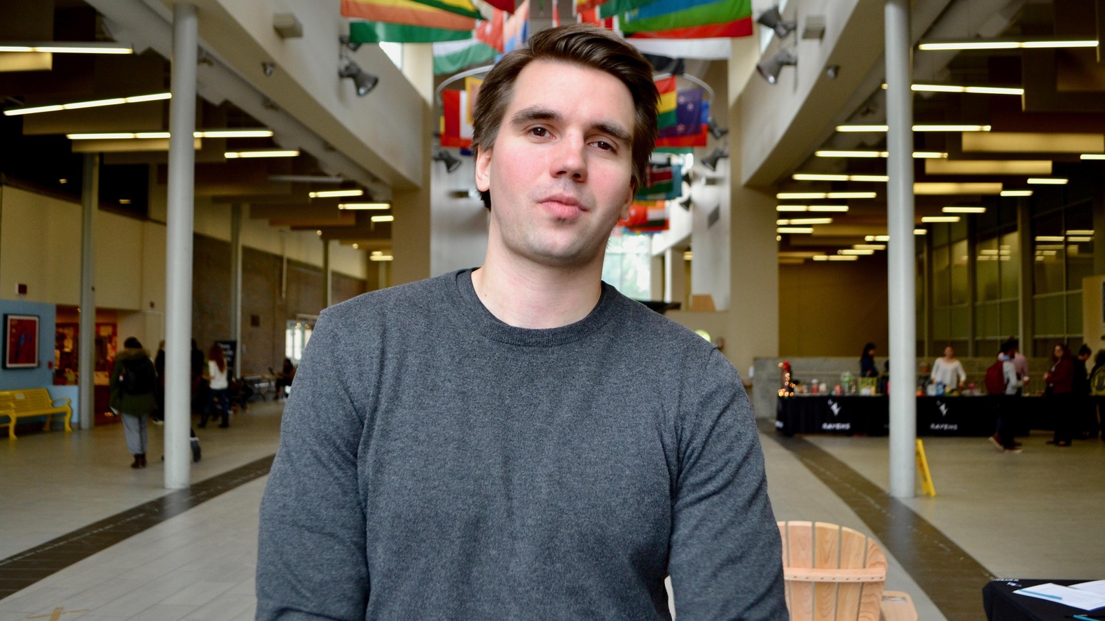 Un jeune homme photographié dans le hall d'une université où sont accrochés les drapeaux de plusieurs pays Un jeune homme photographié dans le hall d'une université où sont accrochés les drapeaux de plusieurs pays