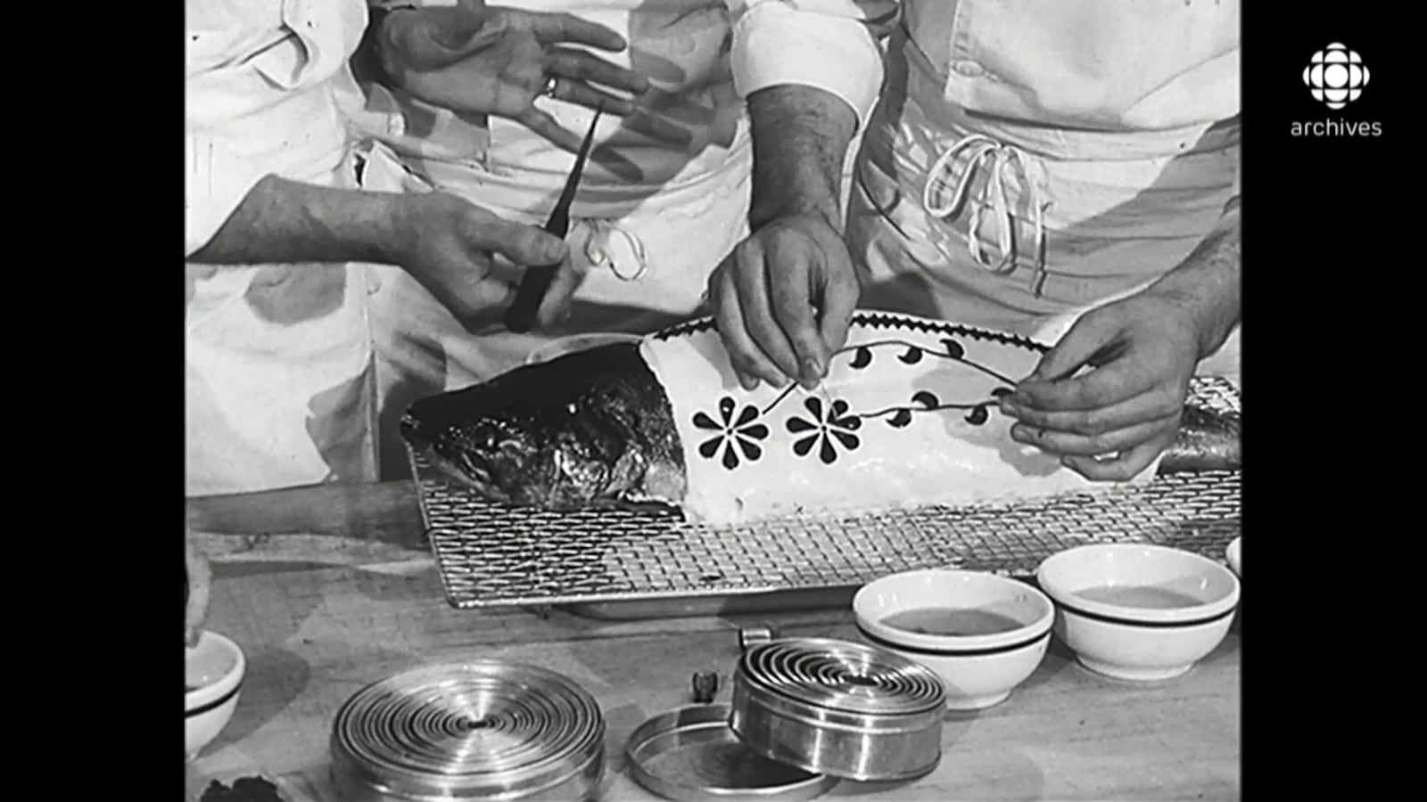 Mains dessinant des fleurs sur la surface d'un poisson entier posé sur une table de préparation en cuisine.