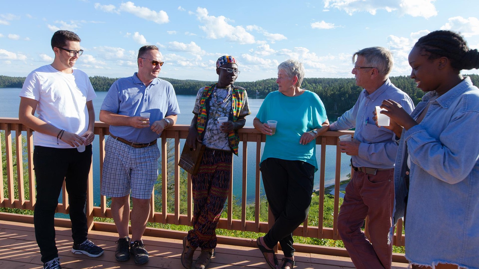 Les six personnes sur un balcon face au lac, un verre à la main Les six personnes sur un balcon face au lac, un verre à la main