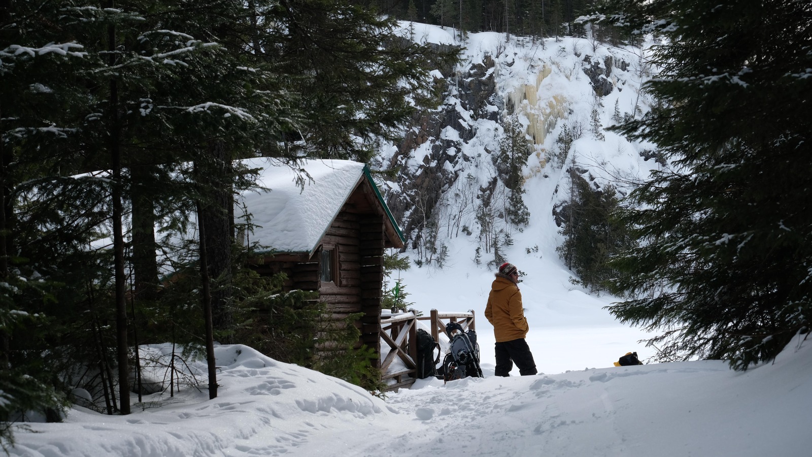 Un homme se tient à proximité d'un chalet. Une paroi glacée est visible à l'arrière-plan. Un homme se tient à proximité d'un chalet. Une paroi glacée est visible à l'arrière-plan.