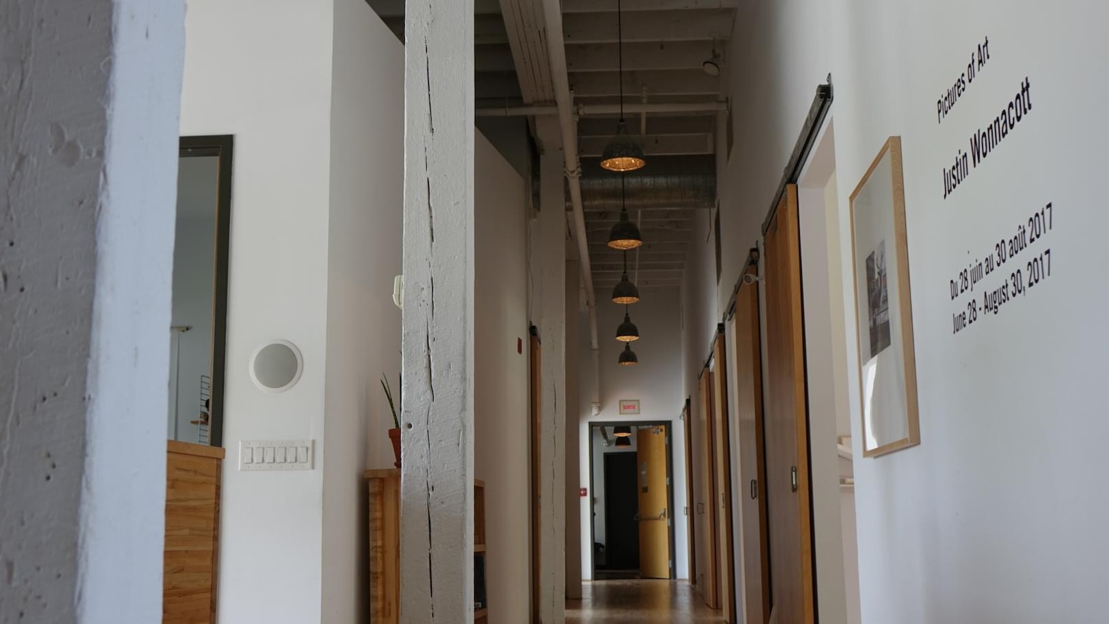 Image montrant un couloir avec plusieurs portes, un plafond haut et des et des luminaires industriels. Image montrant un couloir avec plusieurs portes, un plafond haut et des et des luminaires industriels.